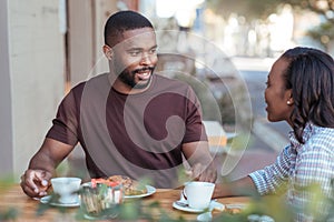 Smiliing young African couple talking together at a sidewalk cafe