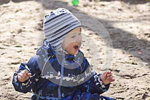 A smiling 2-year- old boy playing in a sandbox