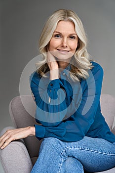 Smiling 50s middle aged woman model sitting in chair looking at camera.