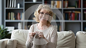 Smiling 60s grandmother enjoy knitting at home