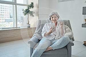 Smiling 60s older senior middle-aged adult lady enjoying mobile for video conference calling virtual family