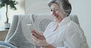 Smiling 60s older senior middle-aged adult lady enjoying mobile for video conference calling virtual family