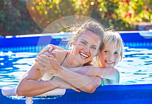 Smiling active mother and child in swimming pool embracing