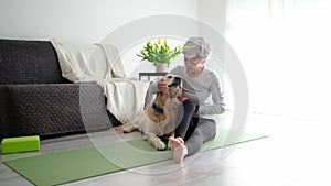 Smiling Active Senior Woman Stroking Her Golden Retriever Dog On A Yoga Mat At Home