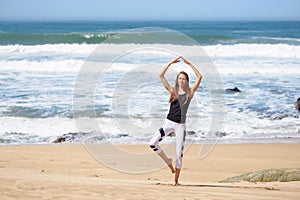 Smiling active young woman doing yoga on the beach