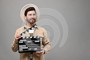 Smiling actor holding clapperboard on grey background, space for text