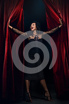 Smiling actress Opening Red Curtain Performing, Woman in Elegant black Dress, on stage