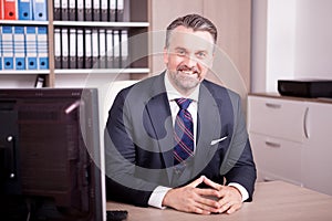 Smiling adult CEO at his desk in office