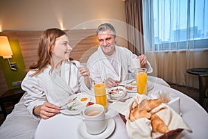 Smiling adult couple having breakfast and looking at each other in hotel room