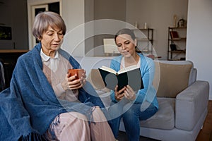 Smiling adult daughter reading for old mother with mental disorder