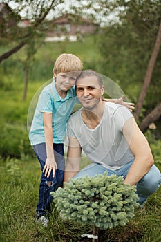 Smiling adult father and his son planting a tree outdoors in park.