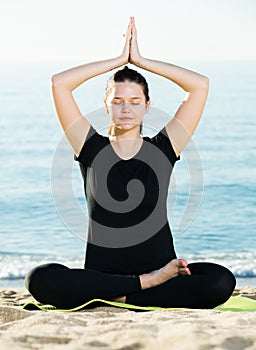 Smiling adult female in black T-shirt is sitting and practicing pranayama
