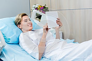 smiling adult female patient using digital tablet on bed photo