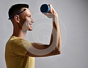 Smiling adult man in t-shirt holds toothbrush behind his ear and a dumbbell in hand looks at copy space. Side view