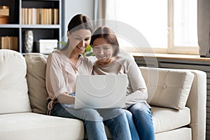 Smiling adult mom and daughter using laptop together
