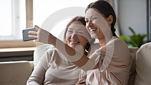 Smiling adult mother and daughter posing for selfie on cell