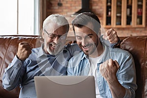 Smiling adult son and old father celebrate online win
