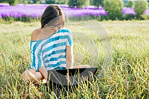 Smiling adult woman with glasses casual clothes using laptop computer sitting on grass on nature, background sunny summer day