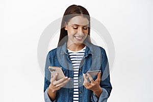 Smiling adult woman looking at her credit card, holding smartphone, paying for purchase, make order on mobile phone app