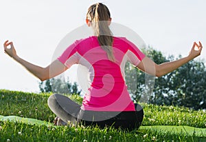 Smiling adult woman in pink T-shirt is sitting her back and practicing meditation