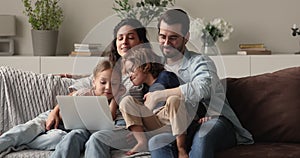 Smiling affectionate young family couple using computer with little kids.