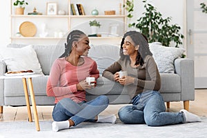 Smiling african american besties having conversation while drinking coffee