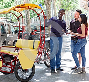 Smiling African-American bikecab driver talking to young couple photo