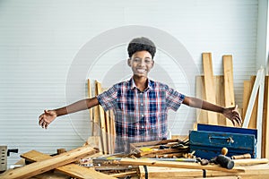 Smiling African-American boy carpenter spreading arms happily to show that the woodwork is placed on the table will try to succeed