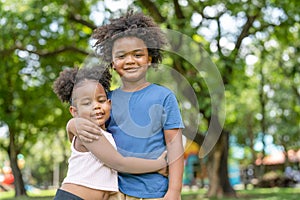 Smiling African American boy and little girl hugging together in park.Happy lovely kid young sister embrace her brother.Family and