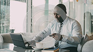 Smiling African American businessman in formal clothes paying online bill using his credit card and laptop in