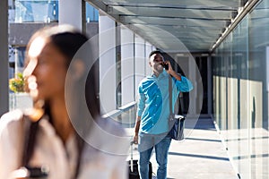 Smiling african american businessman with luggage talking on mobile phone at airport corridor