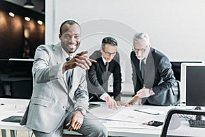 smiling african american businessman pointing away while business colleagues discussing work