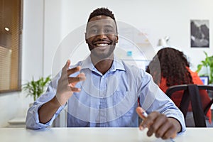 Smiling african american businessman sitting at desk making video call in modern office