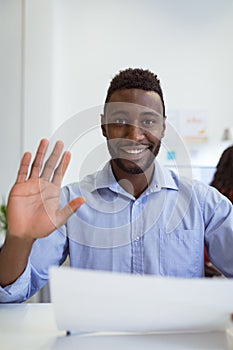 Smiling african american businessman sitting at desk making video call waving in modern office