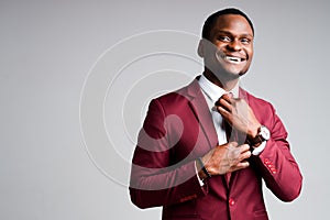 Smiling african american businessman straightens tie around neck and looking at camera