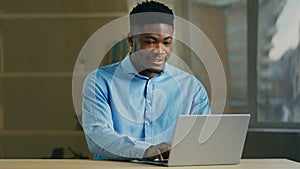 Smiling African American businessman use computer at office. Male professional manager typing on laptop business man