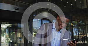 Smiling african american businessman using smartphone outside of modern office building