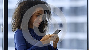 Smiling african american businesswoman texting mobile phone internet in office.