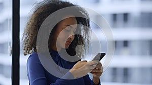 Smiling african american businesswoman texting mobile phone internet in office.