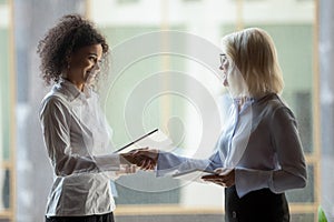 Smiling diverse businesswomen shake hands greeting in office photo