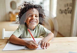 Smiling african american child school boy doing homework while sitting at desk at home