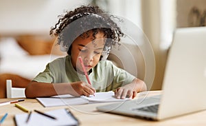 Smiling african american child school boy in headphones studying online on laptop at home