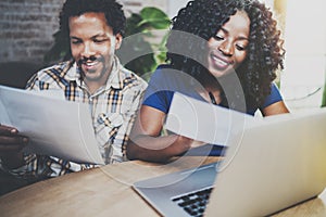 Smiling African american couple checking bills together at the wooden table.Young black man and his girlfriend using