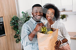 Smiling african american couple holding paper bag with fruits