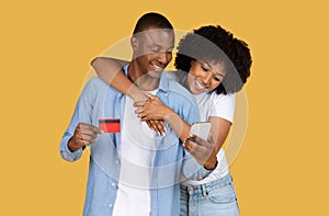 Smiling African American couple making online purchase using credit card and smartphone