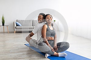 Smiling African American couple relaxing after yoga practice, sitting on fitness mat back to back, smiling at camera