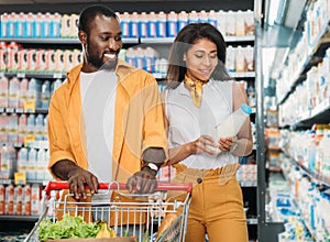 smiling african american couple with shopping trolley choosing milk