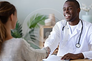 Smiling african American doctor handshake grateful female patient