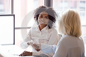 Smiling african American employee handshake colleague greeting at workplace