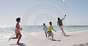 Smiling african american family running and flying kite on sunny beach
